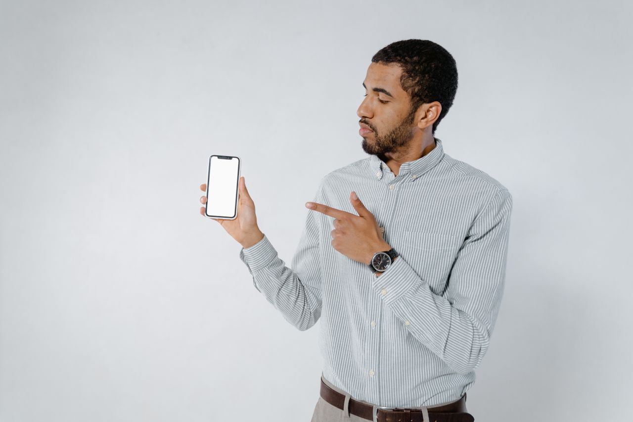 Confident man pointing at smartphone screen against a white background, showcasing technology.